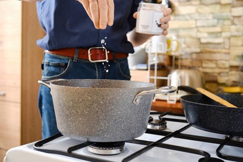 A person is adding sea salt into a pot on a gas stove in a modern kitchen