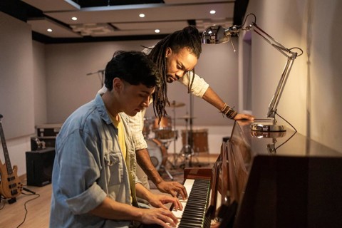 Two musicians work together at a piano, collaborating creatively in a modern recording studio.