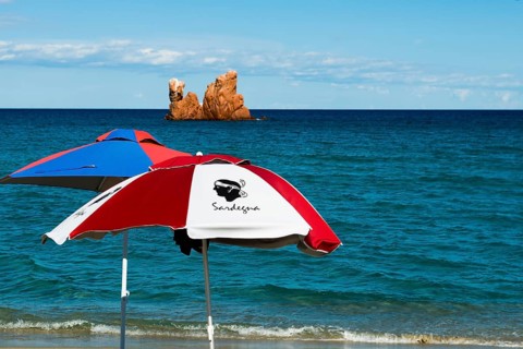 Sunshades on the beach and red rocks, Spiaggia di Cea, Tortoli, Sardinia, Italy