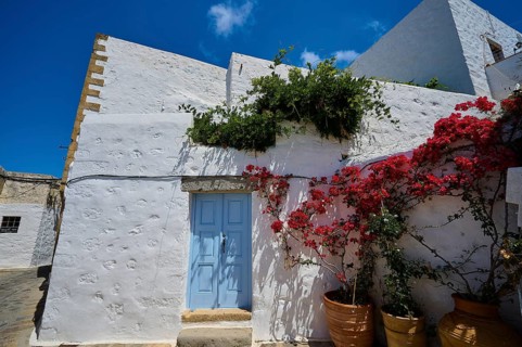 White house with blue door, red flower tendril, bright blue sky, Mediterranean atmosphere, Chora,
