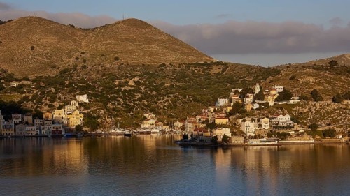 Small village by the water and foot of the hill, bathed in warm sunlight, Symi Town, Symi,