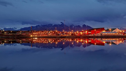 Night view of a city with glowing lights and mountain silhouette reflected in the water, The city