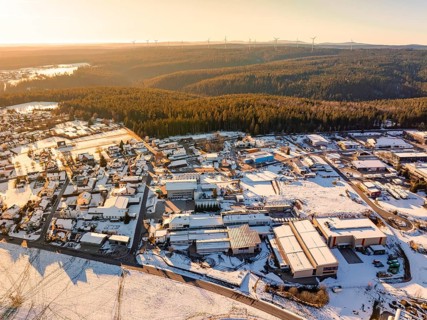 Industrial area next to a forest, with snow-covered roofs and fields under warm evening light,