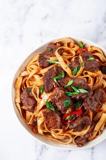 Udon noodles with Mongolian beef, green onions and vegetables, in a white plate, on a light