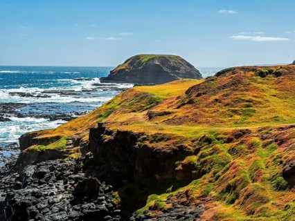 A breathtaking view of rugged coastal cliffs with lush rolling hills extending toward a vibrant