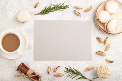Gray paper sheet mockup with cup of coffee, almonds and macaroons on gray concrete background.