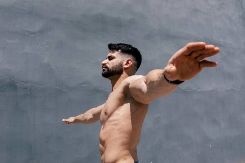 Muscular man with outstretched arms contrasts against a plain gray wall, embodying strength and