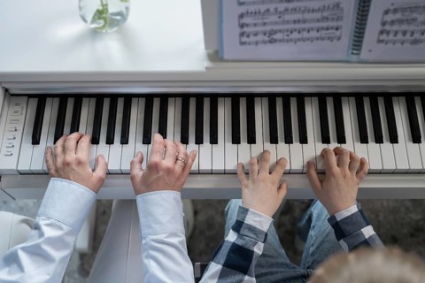 Close-up view of adult and child hands playing the piano together, emphasizing learning and