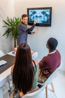 Dentist explaining radiography to young couple in his modern and bright dental clinic, healthcare