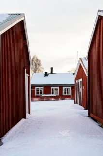 Traditional red wooden buildings in Swedish Lapland under a pale winter sky. Snow covers the