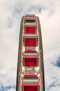 A vertical view of vibrant red Ferris wheel cabins against a soft cloudy backdrop in Hong Kong,