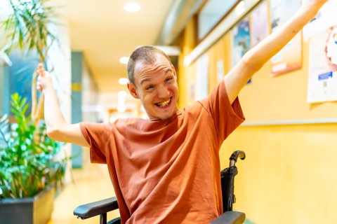 Proud man with disability celebrating in the university sitting on wheelchair and raising arms