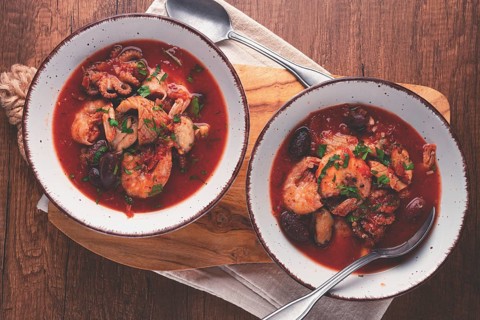 Two plates of seafood in tomato sauce, olives, top view