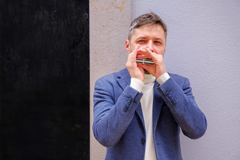 Man musician in a blue blazer and white sweater playing blues on a harmonica with eyes closed,