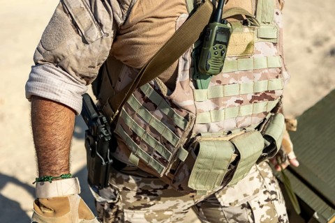 Close up of a man wearing a tactical vest in a desert environment. The camouflage gear is equipped