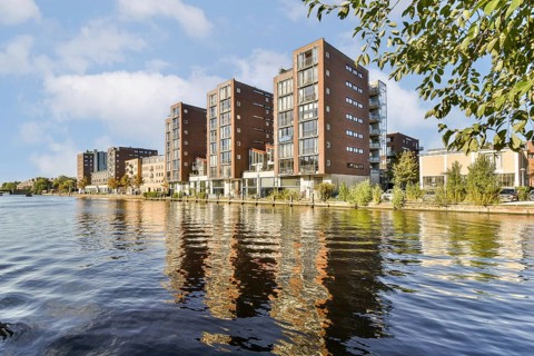 Contemporary apartment buildings line a tranquil waterfront, their reflections shimmering on the