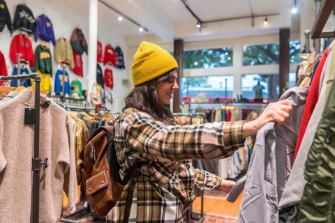 Woman wearing a yellow beanie and plaid shirt looking through a rack of vintage clothing in a