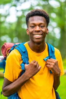 Vertical close-up portrait of a cheerful african backpacker enjoying adventure in natural park
