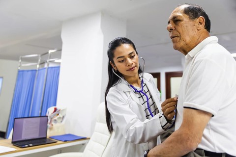 A young female doctor attentively examines an elderly male patient with a stethoscope in a Latin
