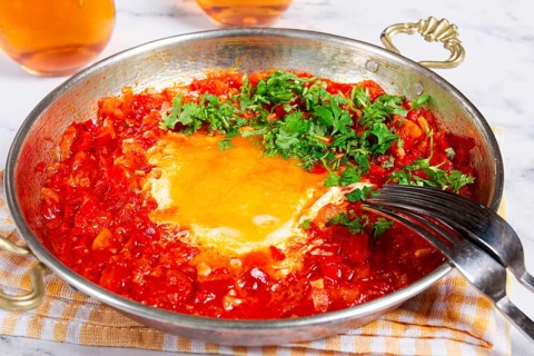 Traditional Turkish dish, scrambled eggs with tomatoes, Menemen, with herbs, in a frying pan,