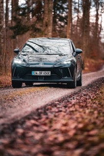 Car driving along a narrow forest path lined with autumn leaves, e-car sharing vehicle from Deer
