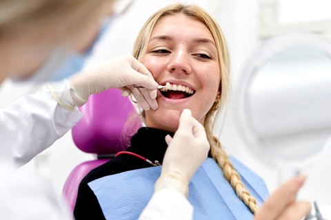 A dentist wearing gloves examines a smiling patient in a modern dental clinic. The patient holds a