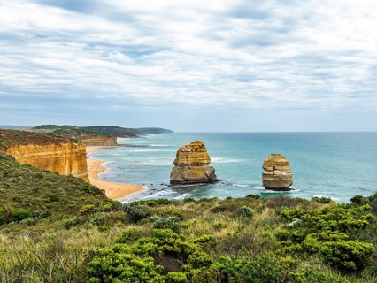 Dramatic coastal rock formations rise from the turquoise ocean, bordered by lush plant life and
