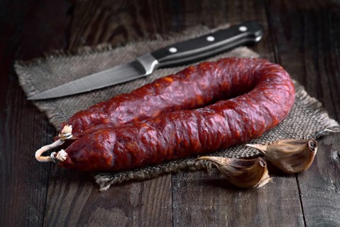 A close-up of a spanish chorizo sausage and garlic cloves on a wooden table A sharp knife adds a