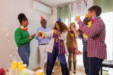 A lively group celebrates a birthday with dancing and laughter. Adorned in colorful hats and leis,