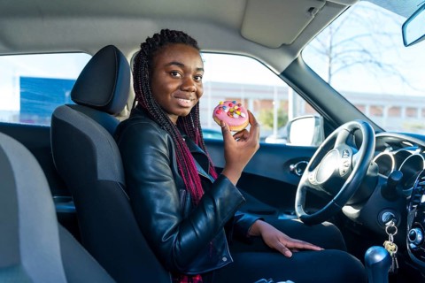 Side view of a happy african woman eating a doughnut sitting on the car