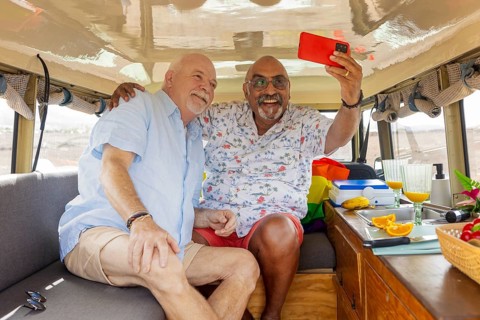 A cheerful elderly gay couple enjoys a moment inside their camper van, capturing a selfie. Both men