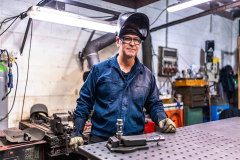 Mature male welder in a metal factory taking a break standing looking at camera
