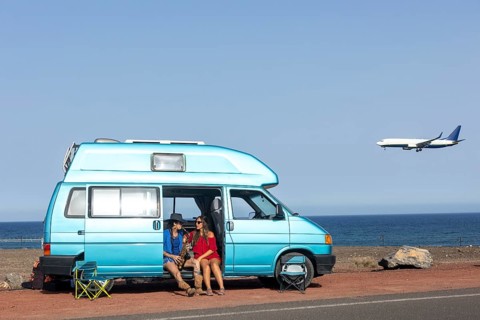 A lesbian couple enjoys a sunny day by their camper van near the ocean. One plays the saxophone