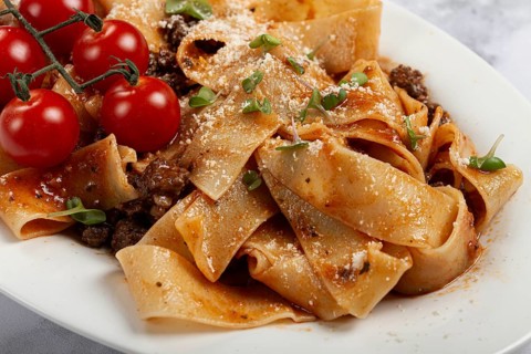 Pappardelle pasta with bolognese sauce, topped with parmesan cheese and cherry branch, homemade, no