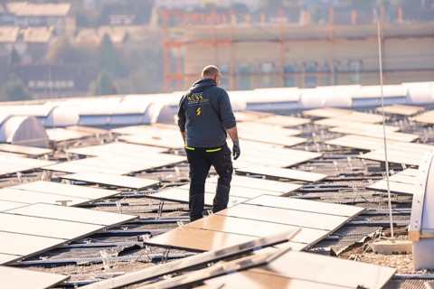 A man is inspecting solar panels on a roof, it is sunny, PV installation at OBI Baumarkt,