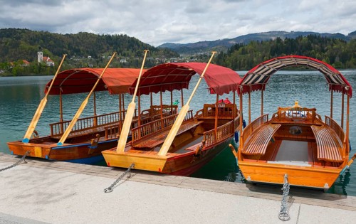 Three wooden boats with red canopies on the lakeshore with mountain backdrop, Lake Bled, Lake