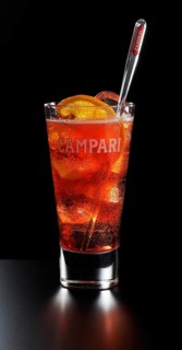 Cocktail Campari Orange Soda in a long drink glass in front of a black background, half an orange