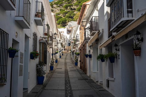 Scenic narrow street with white buildings, balconies, and blue potted flowers in Mijas Pueblo,