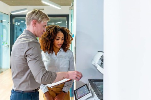 Two colleagues using a modern multifunction printer in a coworking office, enhancing productivity