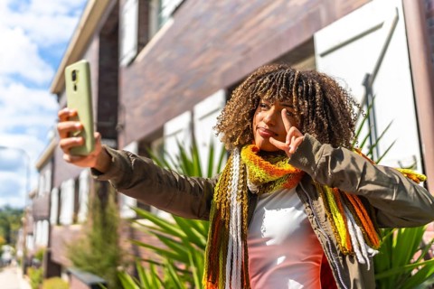 Latin woman gesturing success while taking selfie outdoors standing outside a residential street