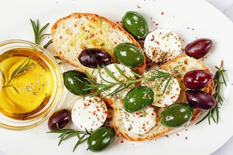 A plate with a snack, ciabatta bread with cheese and olives, olive oil, spices and herbs, top view,