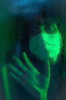 Sad look of a young caucasian brunette with face mask looking at a rainy night in the covid19