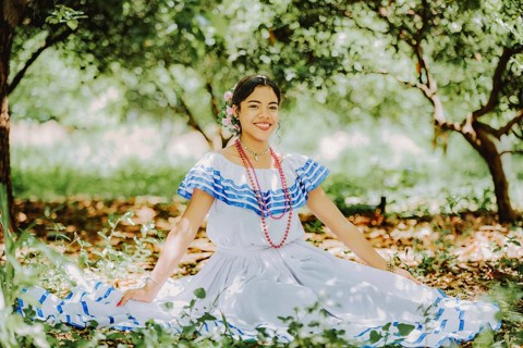 Smiling beautiful girl in national folk costume sitting on the grass