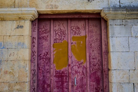 Double pink doors with graffiti on a weathered stone façade, Symi Town, Symi, Dodecanese, Greek