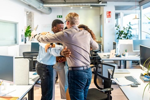 Group of diverse colleagues embracing each other, celebrating a successful project in a modern