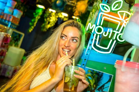 Flirting blonde woman drinking a mojito cocktail in a bar at night