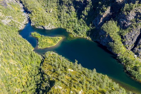 Aerial view of an island in a turquoise colored river surrounded by birch forest, valley