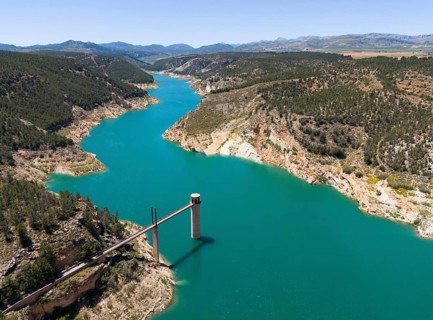 A river with a small bridge or dam surrounded by wooded mountains and rocky shores, aerial view,