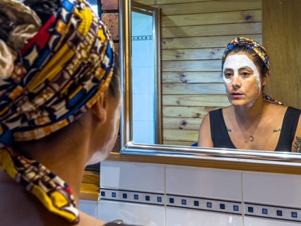 Woman with vibrant headscarf applies a face mask while gazing into a bathroom mirror in Victoria,