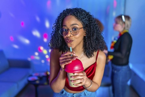 Young woman sipping a beverage through straw, enjoying a vibrant karaoke night with friends,